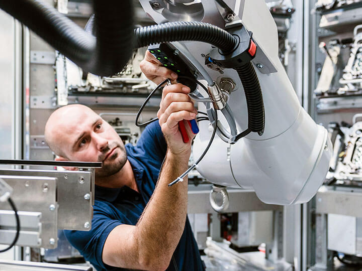 Man with beard and bald head wearing a navy blue polo working on an industrial robot arm in a factory