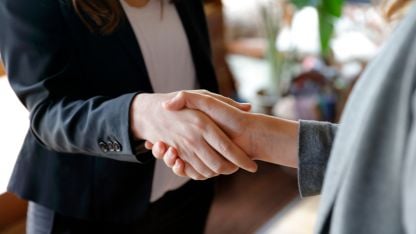 Two business professionals shaking hands in a modern office setting, symbolizing agreement and collaboration.