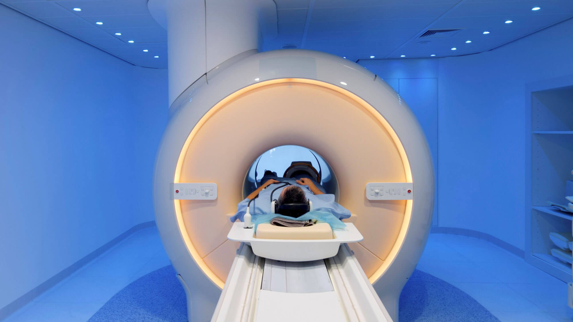 Male medical patient laying inside MRI scanner imaging device in a blue room